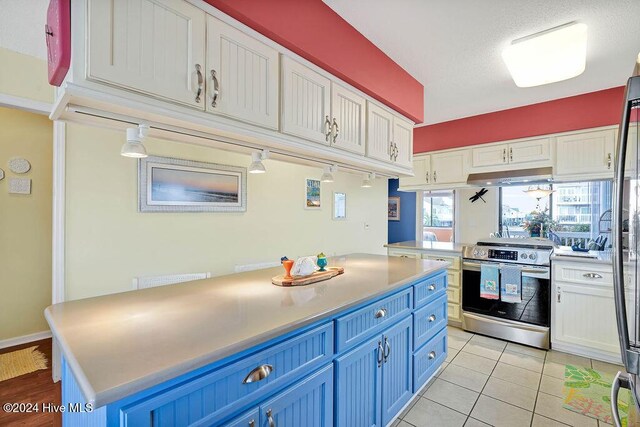 kitchen featuring blue cabinetry, electric range, light tile patterned floors, a kitchen island, and white cabinets