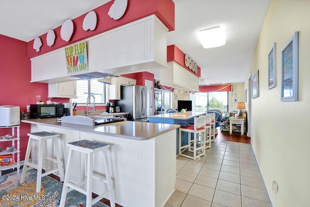 kitchen featuring stainless steel refrigerator, kitchen peninsula, plenty of natural light, and a kitchen bar