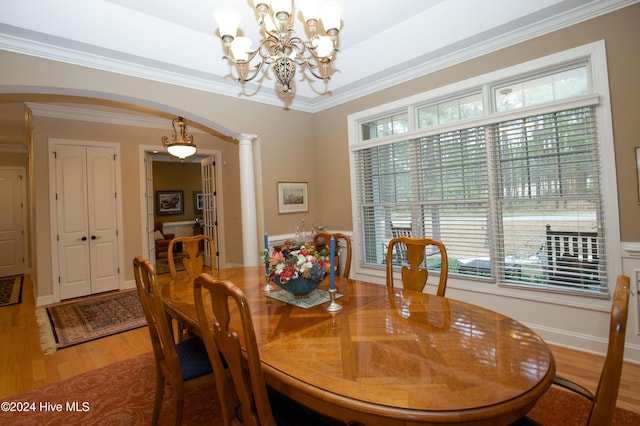 dining area with a notable chandelier, light hardwood / wood-style floors, ornate columns, and crown molding