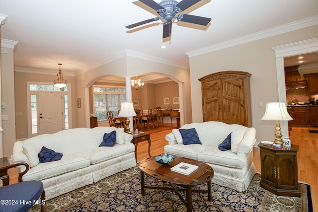 living room featuring ceiling fan with notable chandelier, light wood-type flooring, and crown molding