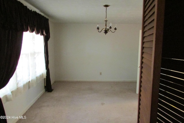 carpeted empty room with an inviting chandelier