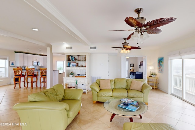 tiled living room with ceiling fan, a healthy amount of sunlight, ornamental molding, and beam ceiling