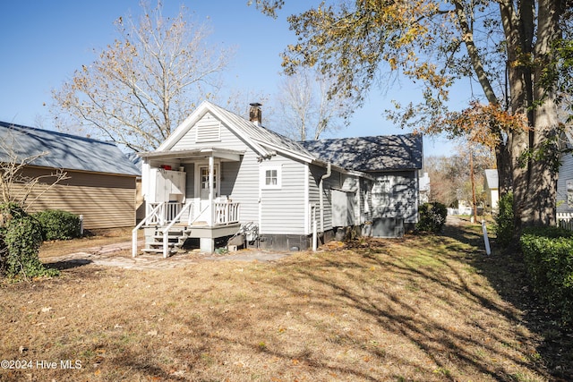 back of house with a yard, covered porch, and a chimney