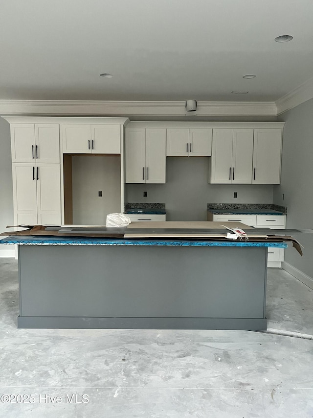 kitchen featuring concrete floors, baseboards, white cabinets, a center island, and crown molding