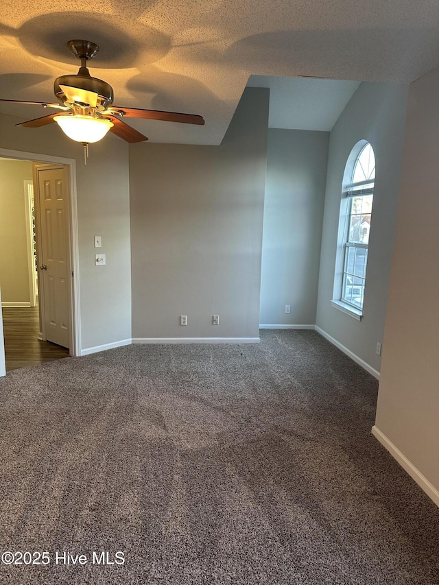 unfurnished room with ceiling fan, dark carpet, and a textured ceiling