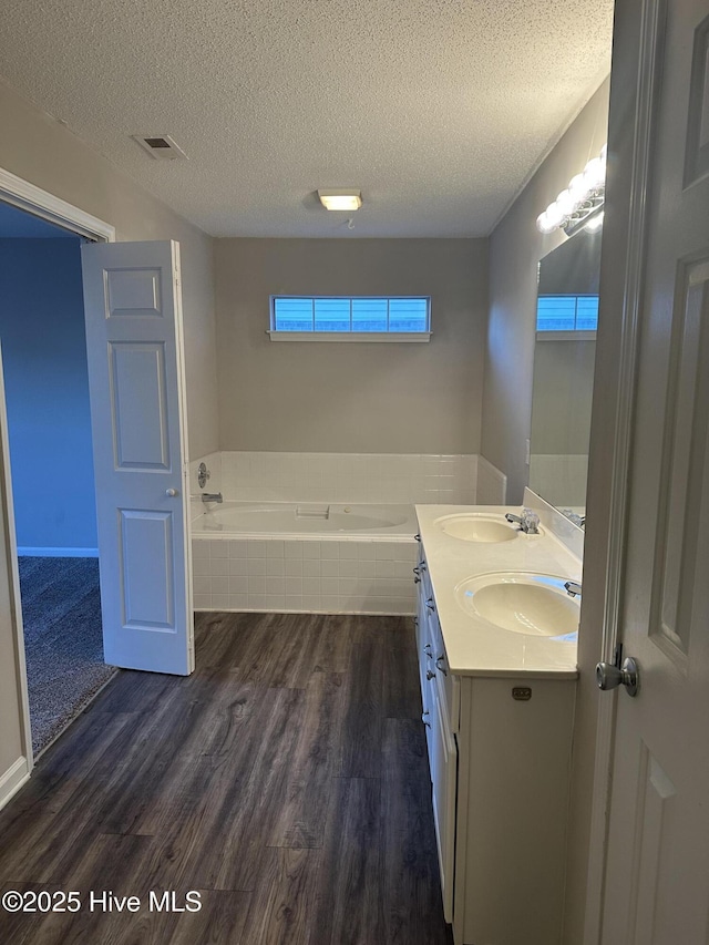 bathroom featuring vanity, a textured ceiling, hardwood / wood-style flooring, and a relaxing tiled tub