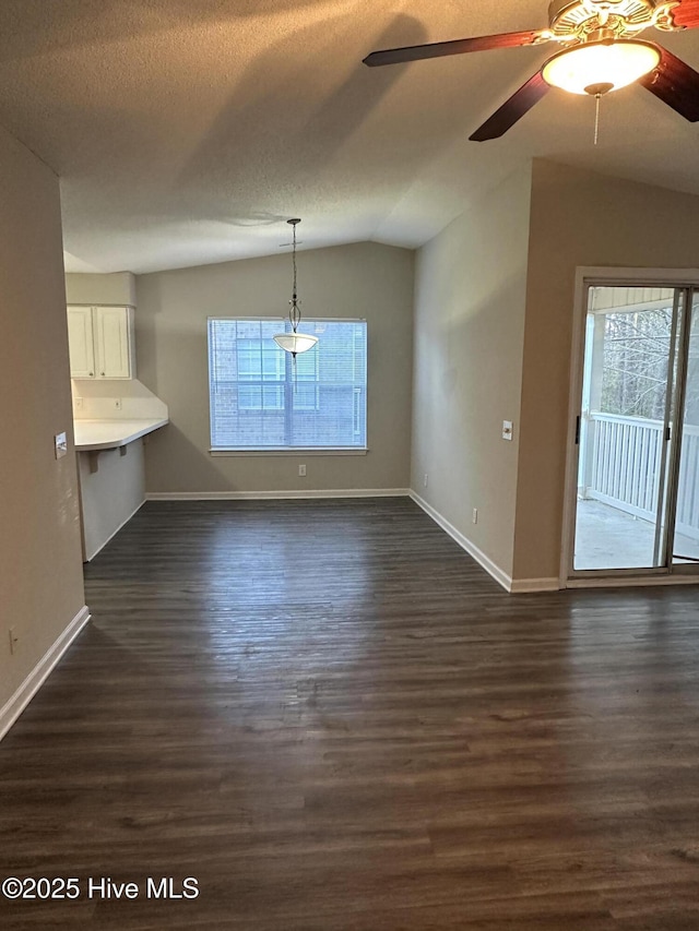 unfurnished dining area with a textured ceiling, dark wood-type flooring, ceiling fan, and lofted ceiling