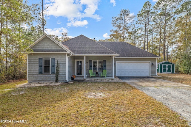 view of front of property featuring a garage, covered porch, a front yard, and a storage shed