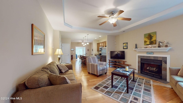 living room featuring a fireplace, light wood-type flooring, a raised ceiling, and ceiling fan