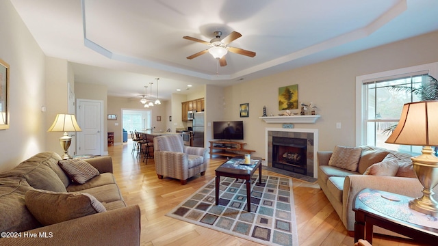 living room with ceiling fan, light hardwood / wood-style floors, a raised ceiling, and a tile fireplace