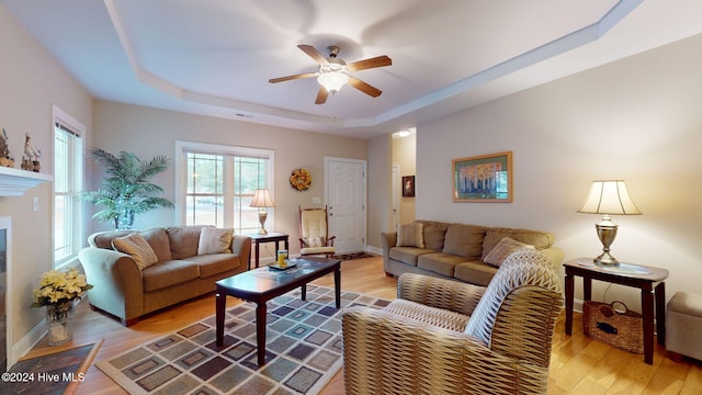 living room featuring ceiling fan, a tray ceiling, and light hardwood / wood-style flooring