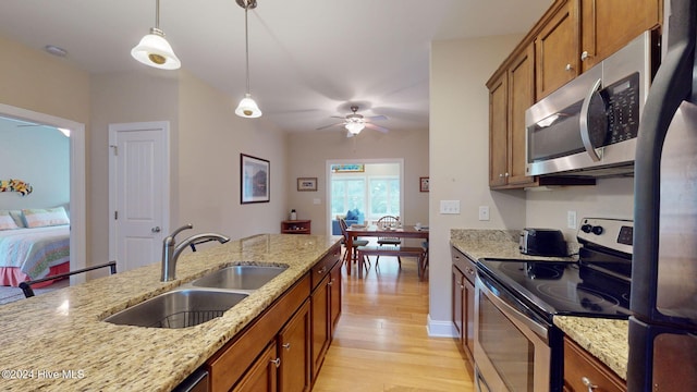 kitchen featuring pendant lighting, sink, light hardwood / wood-style flooring, light stone counters, and stainless steel appliances