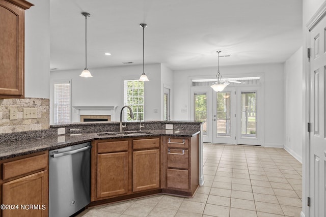 kitchen with decorative light fixtures, stainless steel dishwasher, dark stone counters, and sink