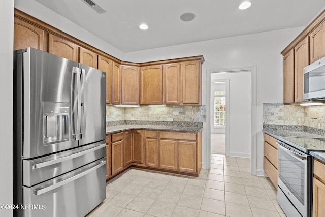 kitchen with decorative backsplash, light tile patterned floors, appliances with stainless steel finishes, and dark stone counters