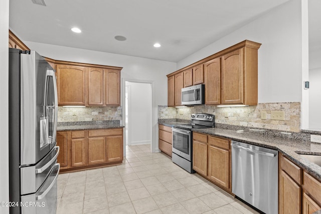 kitchen with tasteful backsplash, dark stone countertops, light tile patterned flooring, and stainless steel appliances