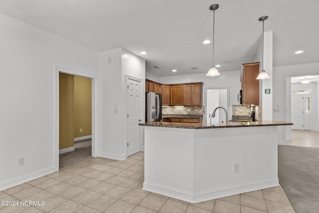 kitchen featuring stainless steel refrigerator with ice dispenser, backsplash, dark stone counters, pendant lighting, and light tile patterned flooring