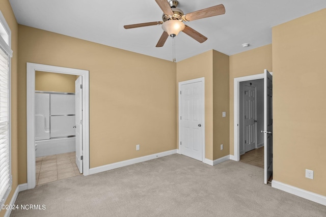 unfurnished bedroom with connected bathroom, light colored carpet, multiple windows, and ceiling fan