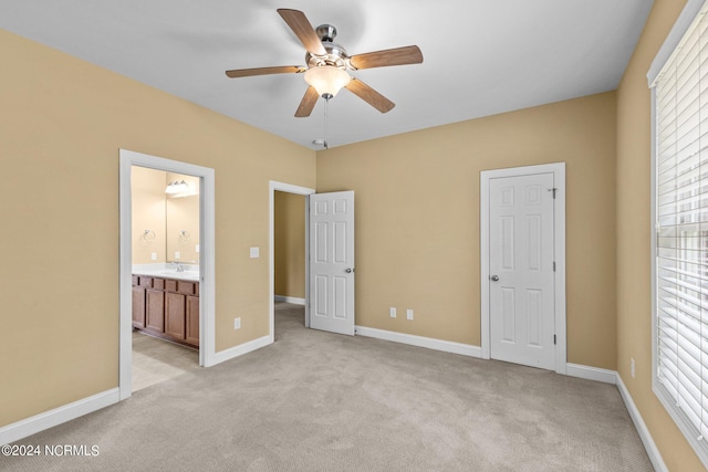 unfurnished bedroom featuring ceiling fan, ensuite bathroom, light colored carpet, and sink