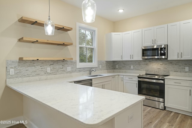 kitchen with decorative light fixtures, kitchen peninsula, white cabinets, and appliances with stainless steel finishes