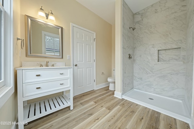 bathroom with hardwood / wood-style flooring, tiled shower, vanity, and toilet