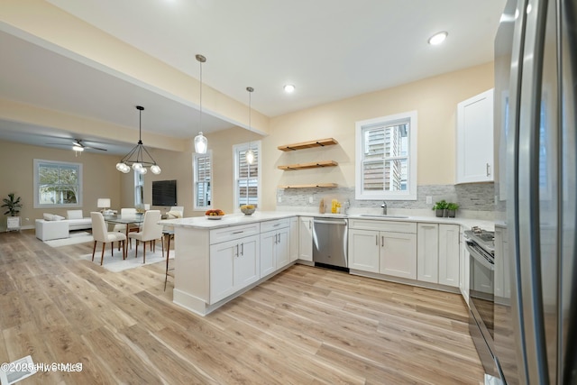 kitchen with sink, hanging light fixtures, stainless steel appliances, white cabinets, and kitchen peninsula