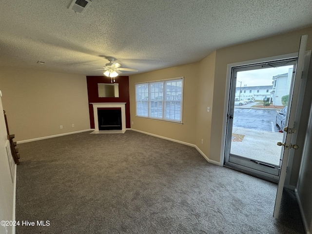 unfurnished living room featuring a textured ceiling, a large fireplace, dark carpet, and ceiling fan