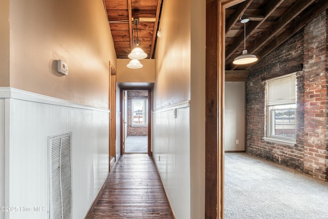 corridor featuring wood ceiling, a towering ceiling, brick wall, beam ceiling, and hardwood / wood-style floors