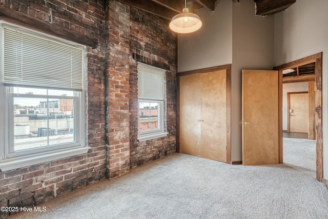 unfurnished bedroom with beamed ceiling, brick wall, carpet flooring, and a high ceiling