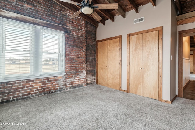 unfurnished bedroom featuring beam ceiling, brick wall, light carpet, wooden ceiling, and multiple closets