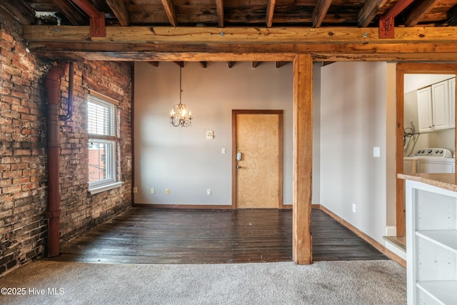 unfurnished dining area featuring dark wood-type flooring, an inviting chandelier, washer and dryer, brick wall, and beam ceiling