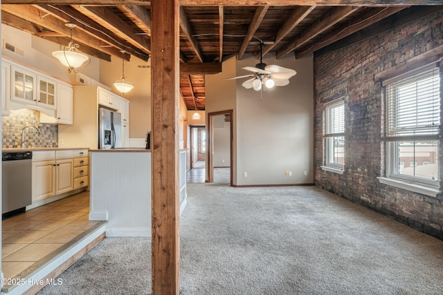 kitchen featuring hanging light fixtures, beam ceiling, a towering ceiling, stainless steel appliances, and brick wall