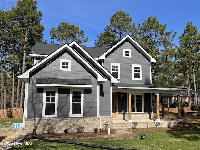 view of front of house with a porch, roof with shingles, a front lawn, and brick siding