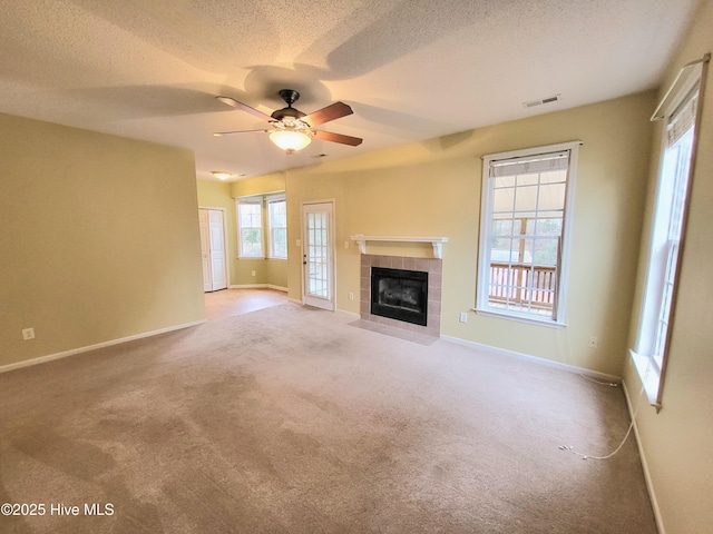 unfurnished living room featuring ceiling fan, carpet floors, a textured ceiling, and a tile fireplace