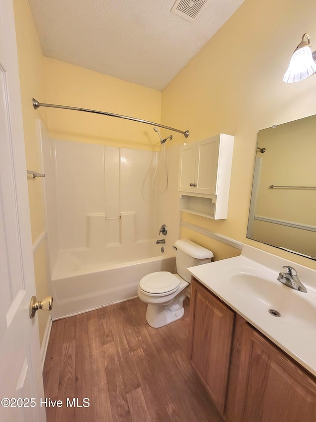 full bathroom featuring hardwood / wood-style floors, vanity,  shower combination, toilet, and a textured ceiling