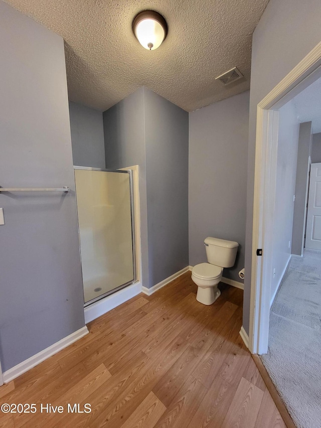 bathroom with hardwood / wood-style floors, toilet, a textured ceiling, and an enclosed shower