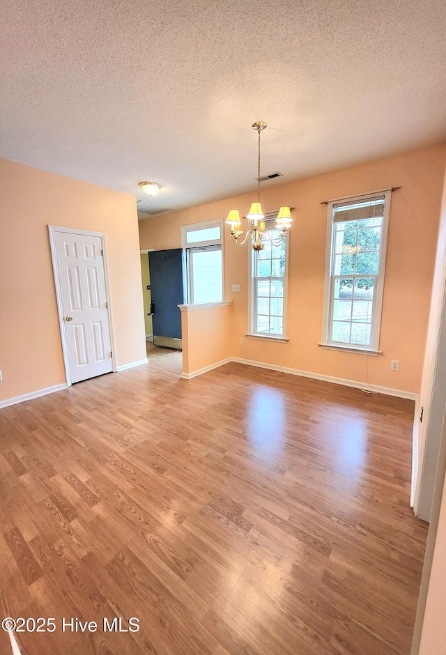 empty room with a notable chandelier, wood-type flooring, and a textured ceiling