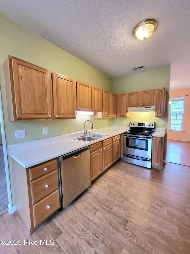 kitchen with a textured ceiling, light hardwood / wood-style floors, sink, and stainless steel appliances