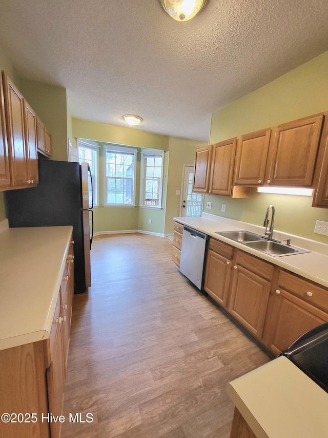 kitchen with a textured ceiling, light hardwood / wood-style flooring, stainless steel dishwasher, and sink