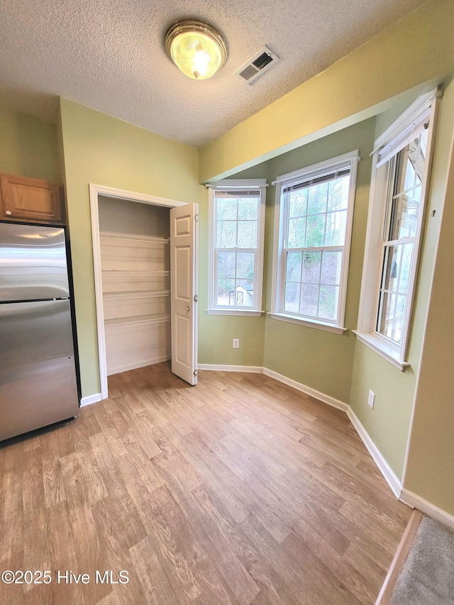 unfurnished bedroom with stainless steel refrigerator, a closet, light hardwood / wood-style floors, and a textured ceiling