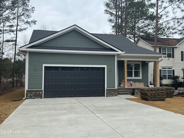 craftsman-style home featuring a shingled roof, concrete driveway, an attached garage, covered porch, and brick siding