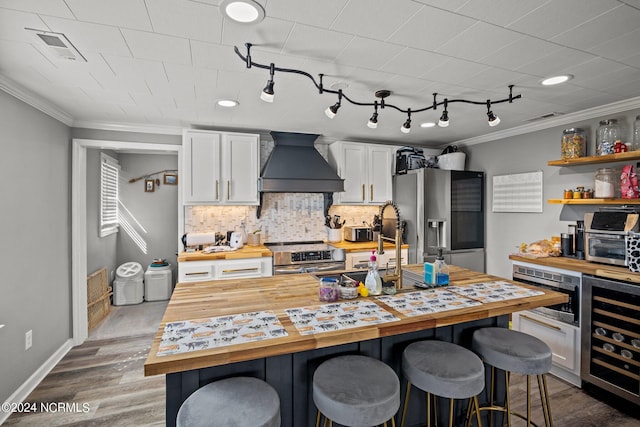 kitchen with wooden counters, premium range hood, stainless steel appliances, white cabinetry, and wine cooler