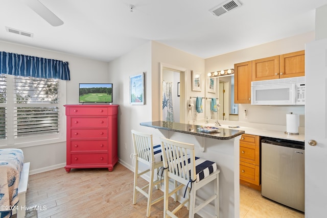 kitchen featuring a breakfast bar, dishwasher, dark stone counters, and light wood-type flooring