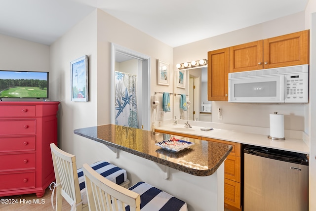 kitchen with dark stone counters, a kitchen breakfast bar, refrigerator, hardwood / wood-style flooring, and kitchen peninsula