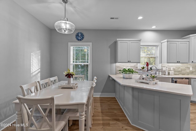 kitchen with tasteful backsplash, light hardwood / wood-style floors, hanging light fixtures, and a healthy amount of sunlight