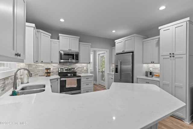 kitchen with backsplash, sink, light hardwood / wood-style floors, white cabinetry, and stainless steel appliances