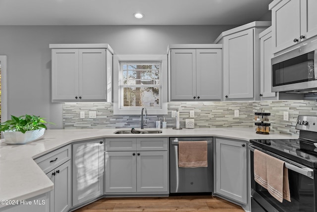 kitchen with backsplash, sink, light hardwood / wood-style flooring, light stone countertops, and appliances with stainless steel finishes