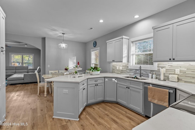 kitchen with kitchen peninsula, stainless steel dishwasher, sink, decorative light fixtures, and light hardwood / wood-style flooring