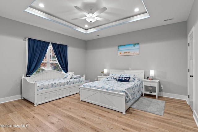 bedroom featuring light wood-type flooring, a raised ceiling, ceiling fan, and ornamental molding