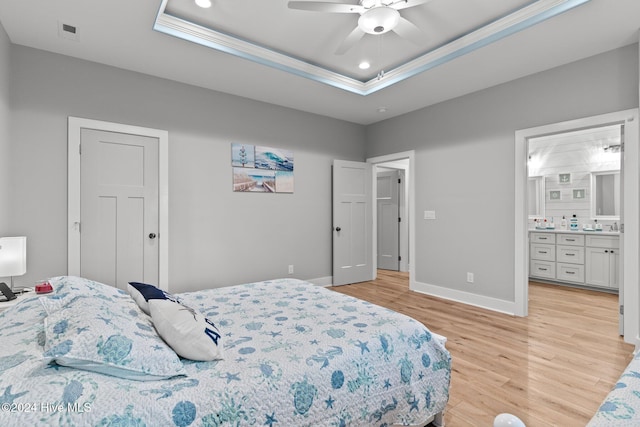 bedroom with a raised ceiling, ensuite bathroom, light hardwood / wood-style flooring, and ceiling fan