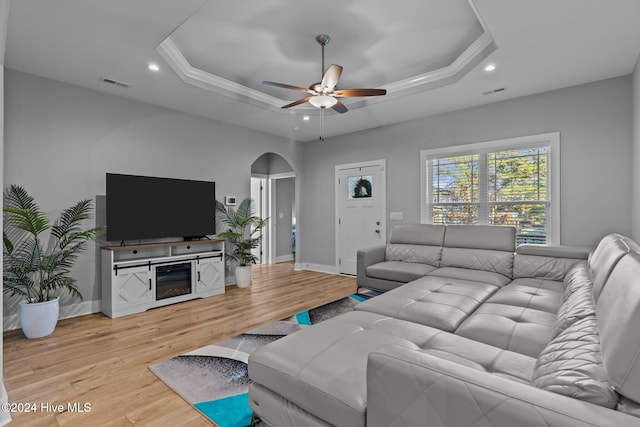 living room with a raised ceiling, light hardwood / wood-style flooring, ceiling fan, and ornamental molding